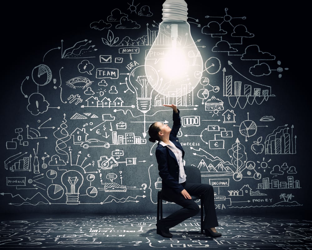 Young businesswoman sitting on chair with big light bulb above